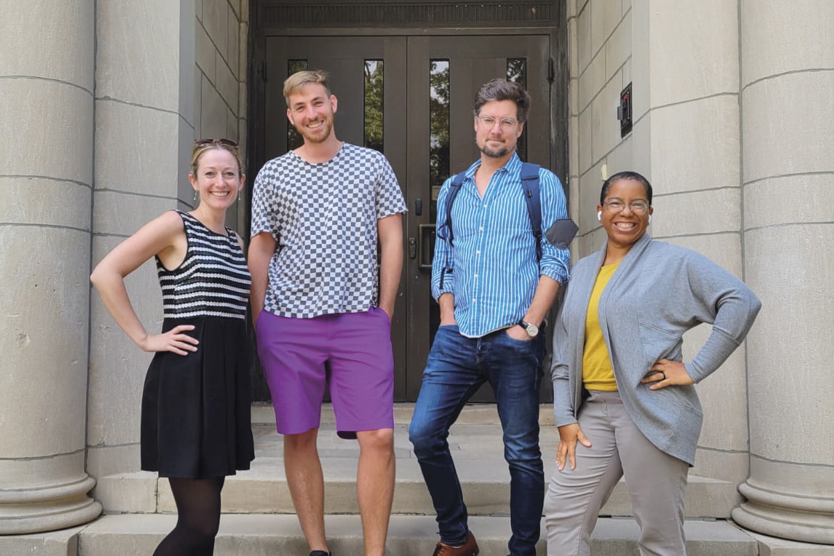 Photo des 4 membres de l'équipe de recherche se tenant debout sur le porche d'un immeuble avec des colonnes de pierre.