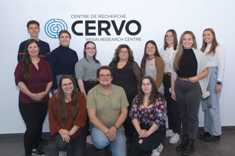 Photo de 12 hommes et femmes se tenant devant un mur avec le logo du Centre de recherche CERVO.