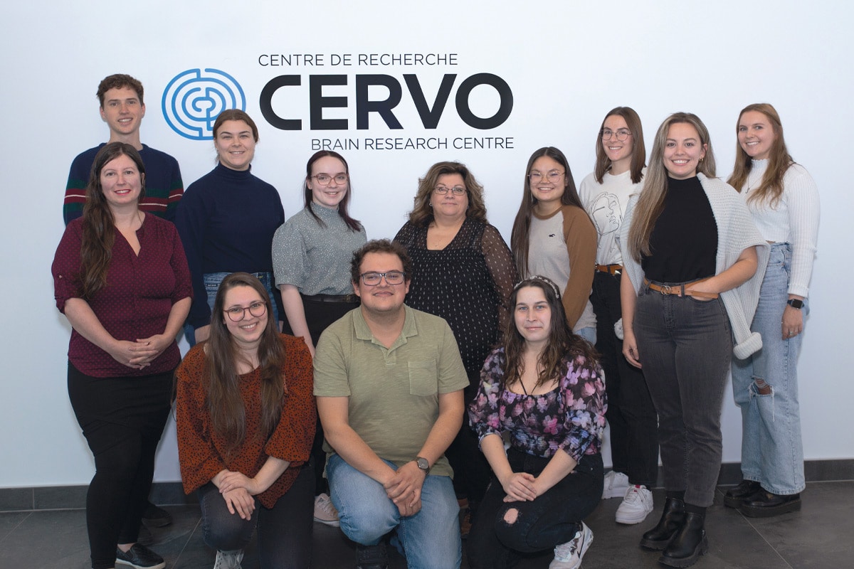 Photo de 12 hommes et femmes se tenant devant un mur avec le logo du Centre de recherche CERVO.