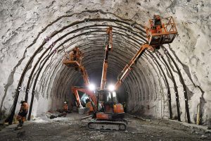 Photo prise à l'intérieur du tunnel. Des engins de chantier dotés de nacelles permettent aux travailleurs de travailler en hauteur sur les parois du tunnel.