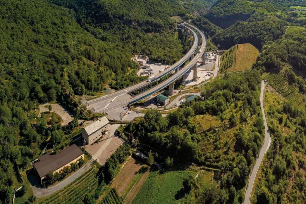 Photo prise du haut des airs. On voit la forêt de chaque côté d'une autoroute sur piliers. Le chantier au pied de ce viaduc.