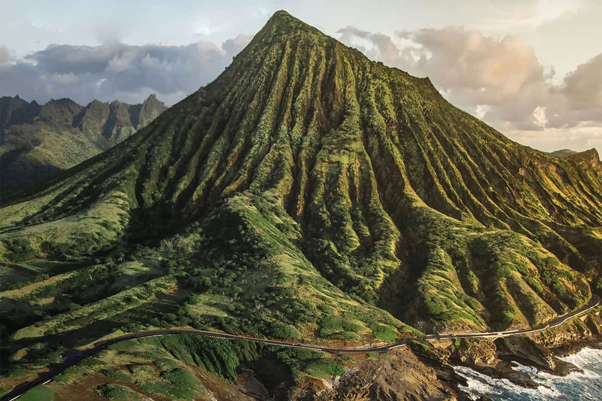 Un volcan aux parois escarpées et découpées de ravins. La végétation le recouvre. Une route serpente à sa base. Les vagues viennent lécher le pourtour de l'île.
