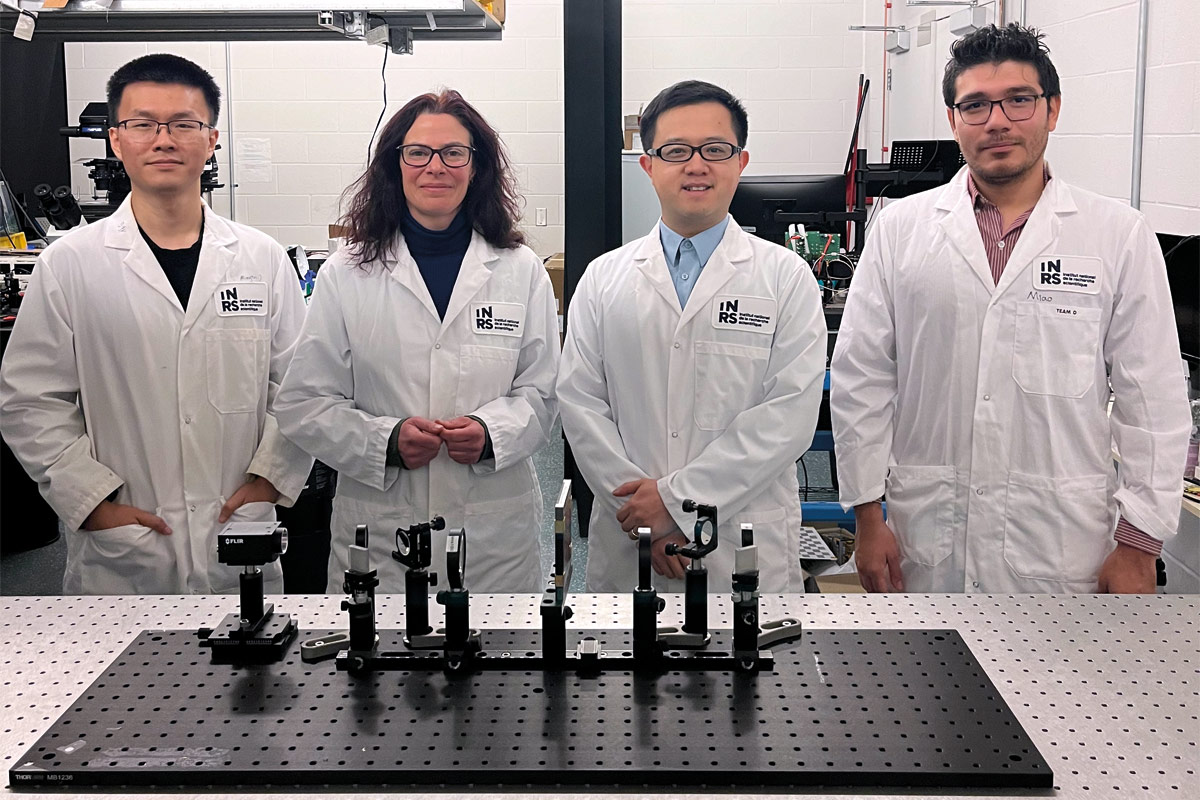 4 personnes en sarrau blanc se tiennent debout derrière un comptoir. À l'avant-plan, on aperçoit un montage expérimental avec divers instruments vissés sur une plaque perforée.